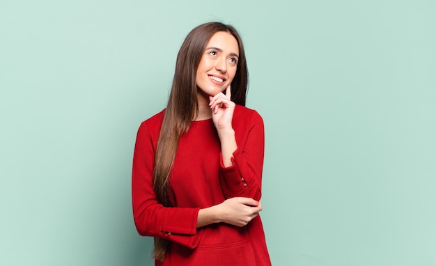 Joven mujer bastante casual sonriendo felizmente y soñando despierto o dudando, mirando hacia un lado