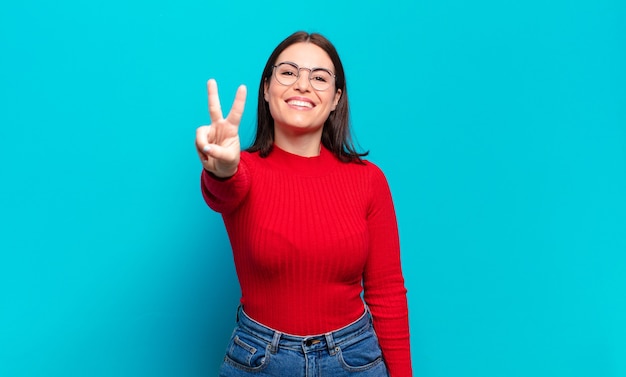 Joven mujer bastante casual sonriendo y luciendo feliz, despreocupada y positiva, gesticulando victoria o paz con una mano