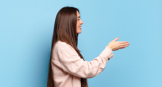 Joven mujer bastante casual sonriendo, saludándote y ofreciendo un apretón de manos para cerrar un trato exitoso, concepto de cooperación