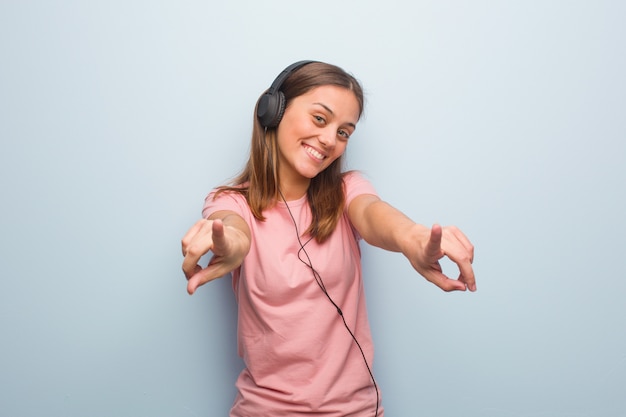 Joven mujer bastante caucásica alegre y sonriente apuntando al frente. Ella está escuchando música con auriculares.