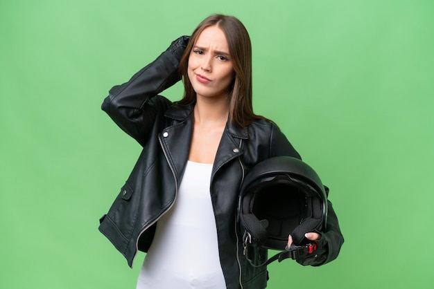 Joven mujer bastante caucásica con un casco de motocicleta sobre un fondo aislado que tiene dudas