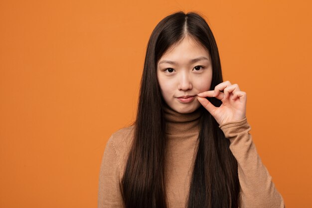 Joven mujer bastante china con los dedos en los labios guardando un secreto.