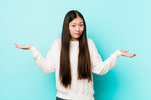 Joven mujer bastante china dudando y encogiéndose de hombros en gesto de cuestionamiento.