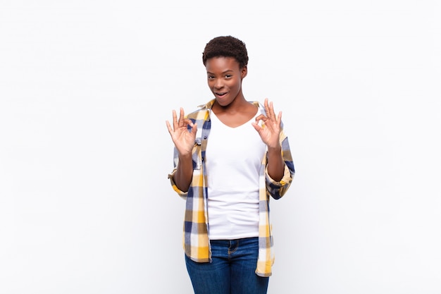 Joven mujer bastante negra sintiéndose conmocionada, asombrada y sorprendida, mostrando aprobación haciendo un signo bien con ambas manos
