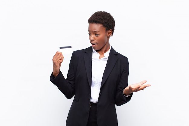 Joven mujer bastante negra sintiéndose extremadamente sorprendida y sorprendida con una tarjeta de crédito