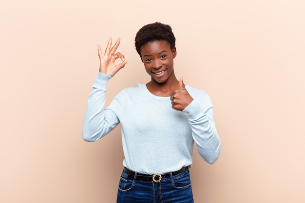 Joven mujer bastante negra sintiéndose feliz, asombrada, satisfecha y sorprendida, mostrando gestos bien y pulgares arriba, sonriendo