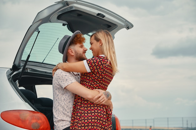 Joven y mujer besándose en el baúl del auto