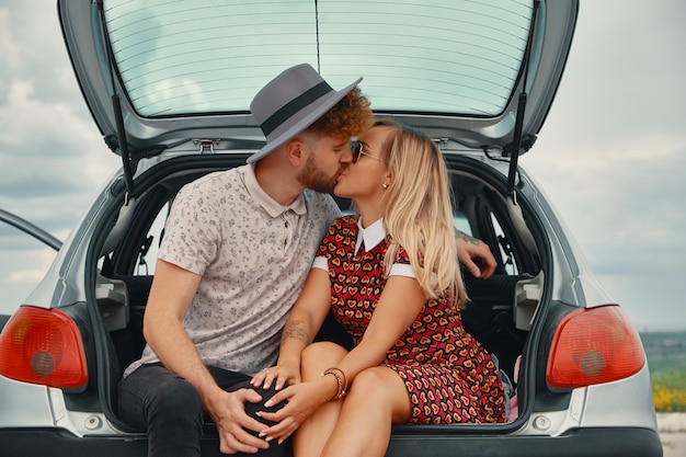 Joven y mujer besándose en el baúl del auto