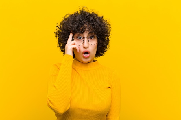 Joven mujer bonita afro que parece sorprendida, con la boca abierta, sorprendida, dándose cuenta de un nuevo pensamiento