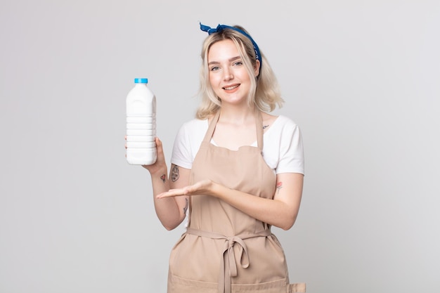 Joven mujer bonita albina sonriendo alegremente, sintiéndose feliz y mostrando un concepto con una botella de leche