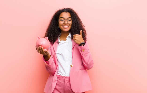 Joven mujer bonita con una alcancía contra la pared rosa