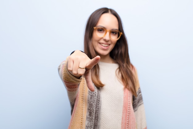 Foto joven mujer bonita apuntando a la cámara con una sonrisa satisfecha, segura y amigable, eligiéndote contra la pared azul