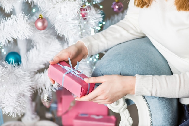 Joven mujer bonita bajo el árbol de año nuevo con regalo de Navidad