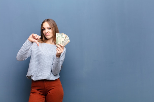 Joven mujer bonita con billetes de dólar contra la pared azul con un espacio de copia