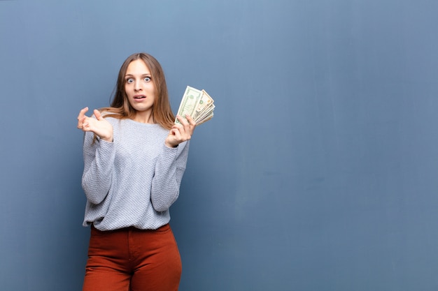 Joven mujer bonita con billetes de dólar contra la pared azul con un espacio de copia