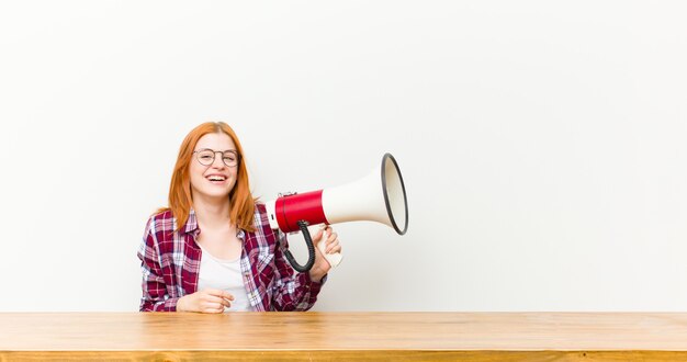 Joven mujer bonita cabeza roja delante de una mesa de madera con un megáfono