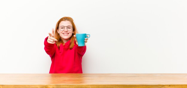 Joven mujer bonita cabeza roja delante de una mesa de madera con una taza de café