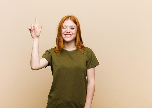 Joven mujer bonita cabeza roja sonriendo alegremente y felizmente, apuntando hacia arriba con una mano para copiar espacio