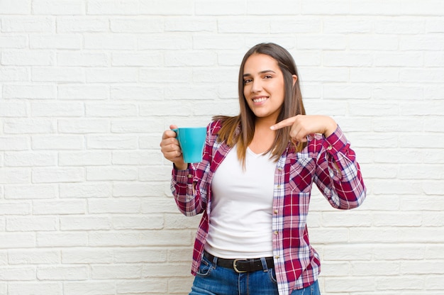 Joven mujer bonita con un café contra la textura de la pared de ladrillo