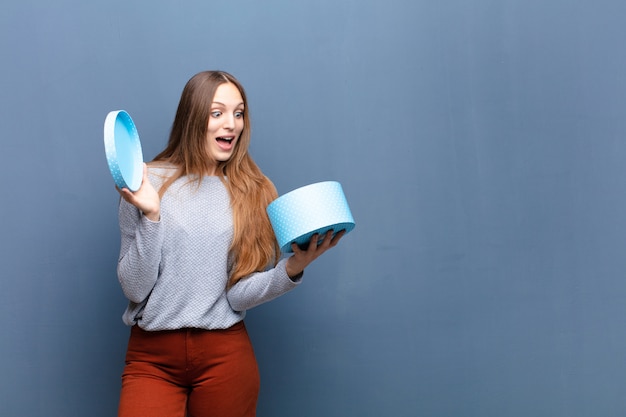 Joven mujer bonita con una caja azul contra la pared azul con un espacio de copia