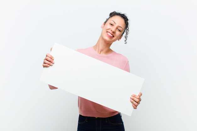 Joven mujer bonita con un cartel contra la pared blanca