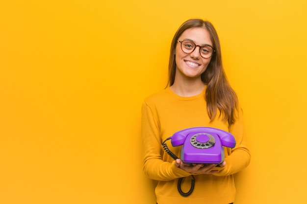 Joven mujer bonita caucásica alegre con una gran sonrisa. Ella está sosteniendo un teléfono antiguo.