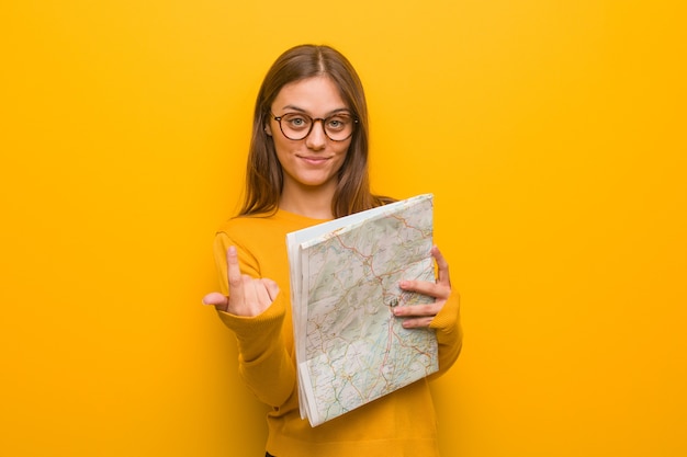 Joven mujer bonita caucásica invitando a venir. Ella sostiene un mapa.