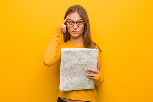 Joven mujer bonita caucásica pensando en una idea. Ella sostiene un mapa.