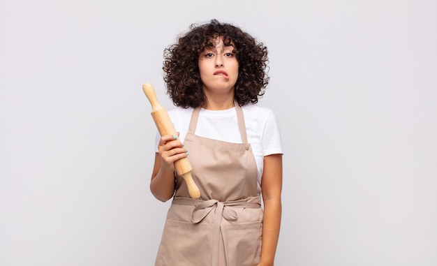 Joven mujer bonita chef mirando desconcertado y confundido, mordiéndose el labio con un gesto nervioso, sin saber la respuesta al problema