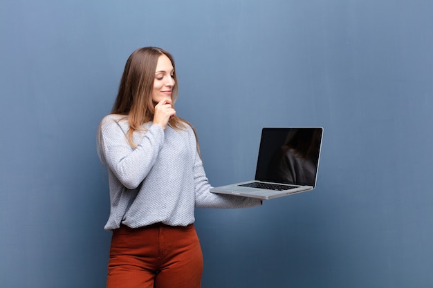 Joven mujer bonita con una computadora portátil contra la pared azul con un espacio de copia