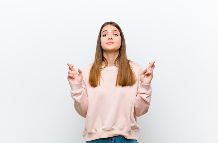 Foto joven mujer bonita cruzando los dedos con ansiedad y esperando buena suerte con una mirada preocupada contra la pared blanca