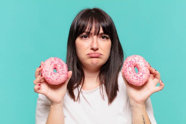 Joven mujer bonita con curvas expresión triste y sosteniendo una rosquilla