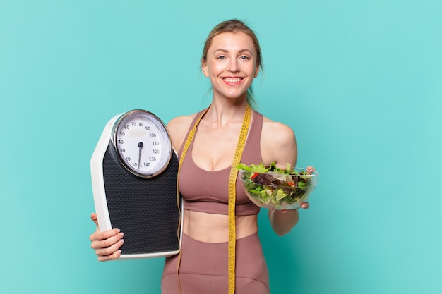 Joven mujer bonita deporte expresión feliz y sosteniendo una balanza y una ensalada