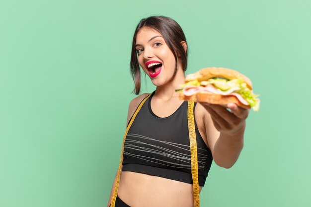 Joven mujer bonita deporte expresión sorprendida y sosteniendo un sándwich