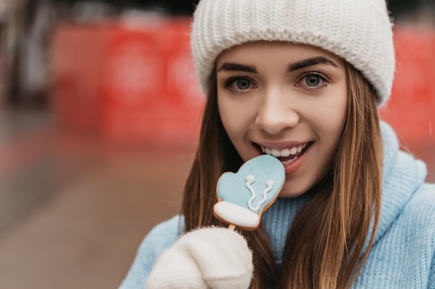 Joven mujer bonita encantadora de pie en la calle comiendo galletas de chocolate dulces de jengibre en un palo