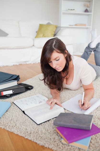 Foto joven mujer bonita escribiendo en un cuaderno mientras está acostado en una alfombra