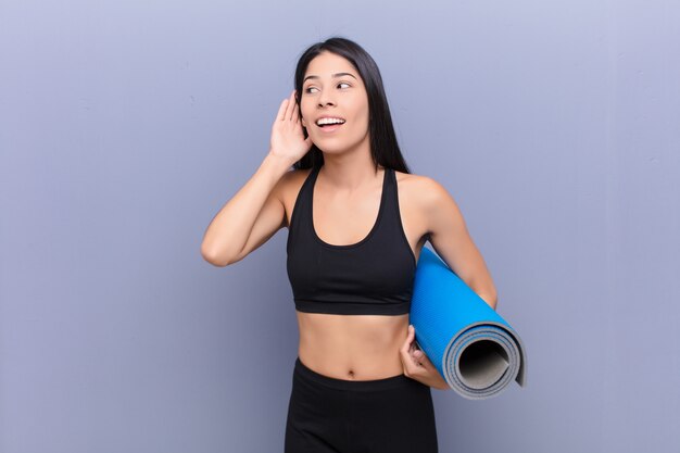 Joven mujer bonita con una estera de yoga contra la pared de cemento