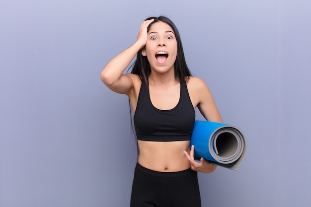 Joven mujer bonita con una estera de yoga contra la pared de cemento