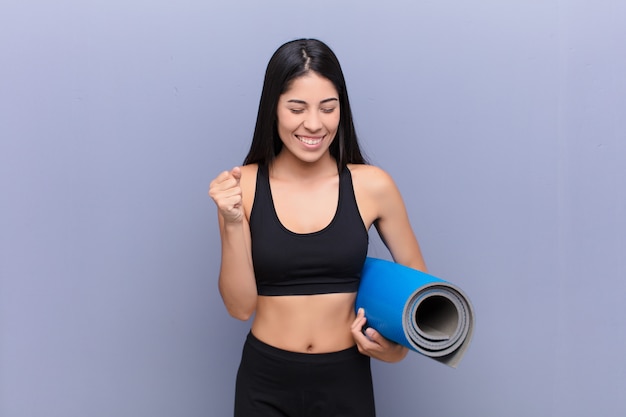 Joven mujer bonita con una estera de yoga contra la pared de cemento