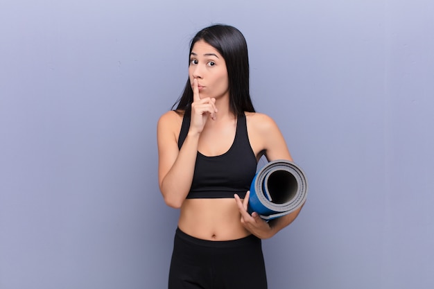 Joven mujer bonita con una estera de yoga contra la pared de cemento