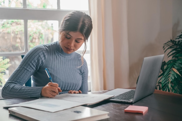 Una joven mujer bonita estudiando y haciendo la tarea en casa en la mesa Adolescente femenina usando una computadora portátil o una computadora navegando por la red interior