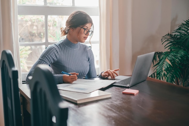 Una joven mujer bonita estudiando y haciendo la tarea en casa en la mesa Adolescente femenina usando una computadora portátil o una computadora navegando por la red interior