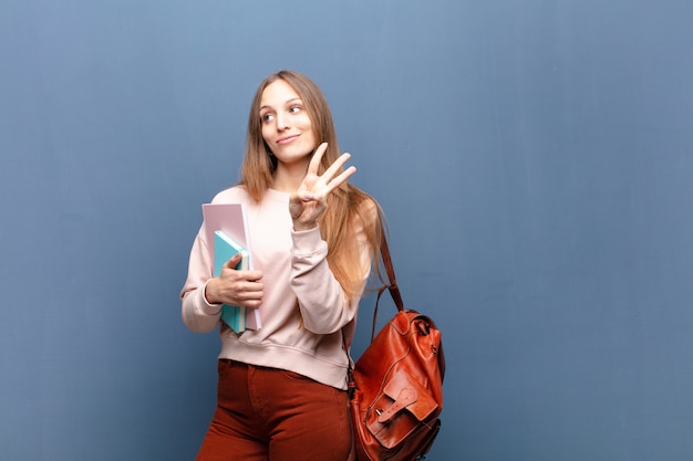 Joven mujer bonita estudiante con libros y bolsa contra azul con un copyspace