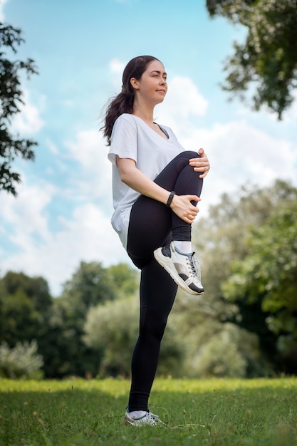 Una joven mujer bonita en forma en ropa deportiva haciendo calentamiento en el parque. Vertical. El concepto de entrenamiento deportivo