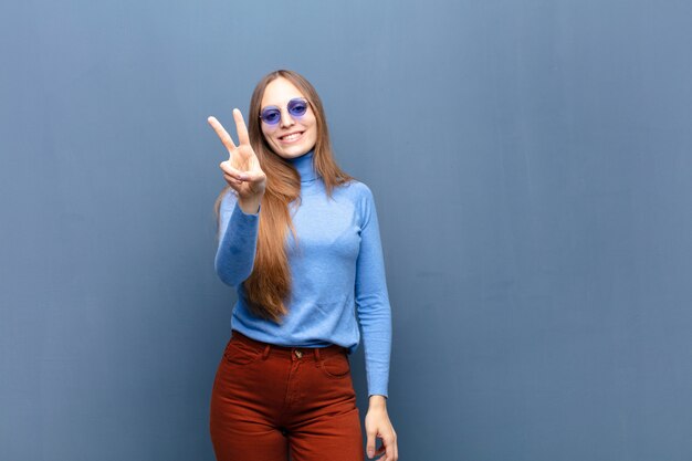 Joven mujer bonita con gafas de sol contra la pared azul con un espacio de copia