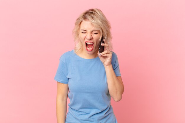 joven mujer bonita gritando agresivamente, luciendo muy enojada. concepto celular