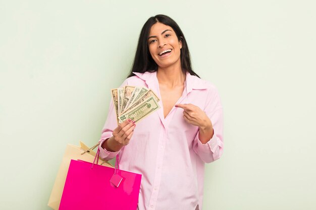 Joven mujer bonita hispana que parece emocionada y sorprendida señalando el concepto de bolsas de compras laterales