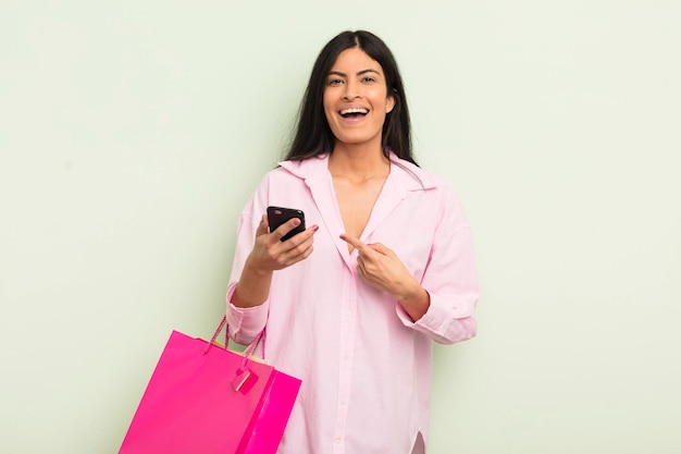 Joven mujer bonita hispana que parece emocionada y sorprendida señalando el concepto de bolsas de compras laterales