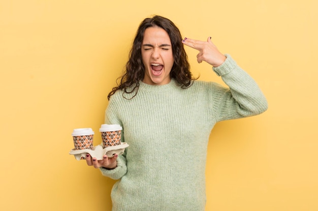 Joven mujer bonita hispana que parece infeliz y estresada gesto de suicidio haciendo el signo de la pistola para llevar el concepto de café