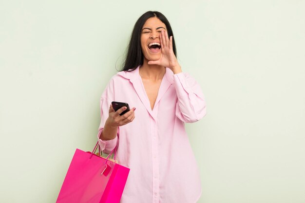 Joven mujer bonita hispana que se siente feliz dando un gran grito con las manos junto a la boca concepto de bolsas de compras